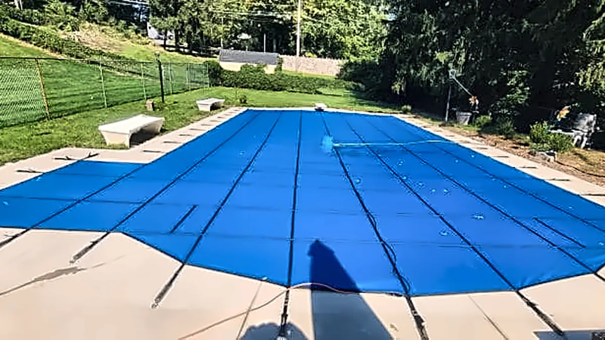 Blue safety cover secured over a closed in-ground pool