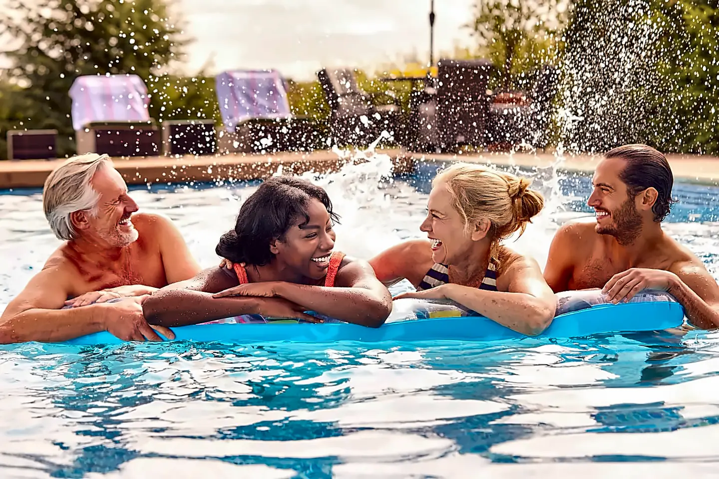 Four adults relaxing in a backyard swimming pool.