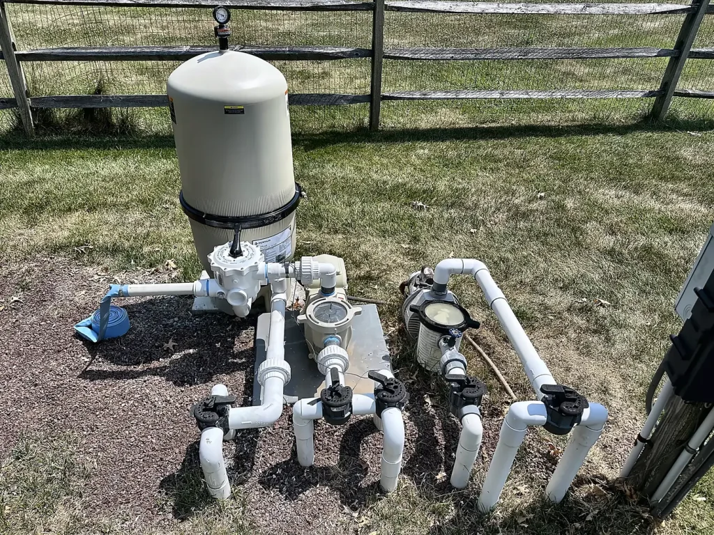 Residential pool filter and pump system installed beside a backyard fence